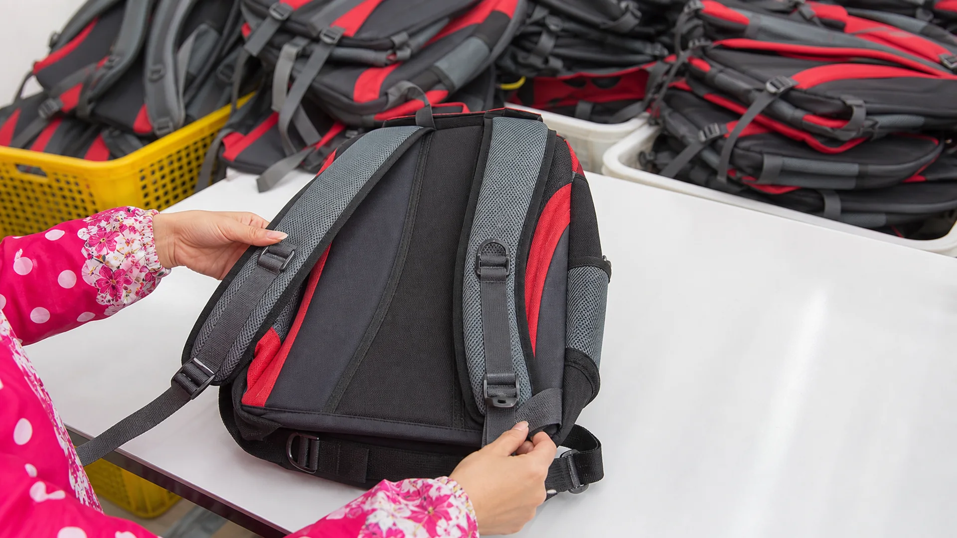 Worker inspecting the shoulder straps and buckles of a complete red and charcoal backpack